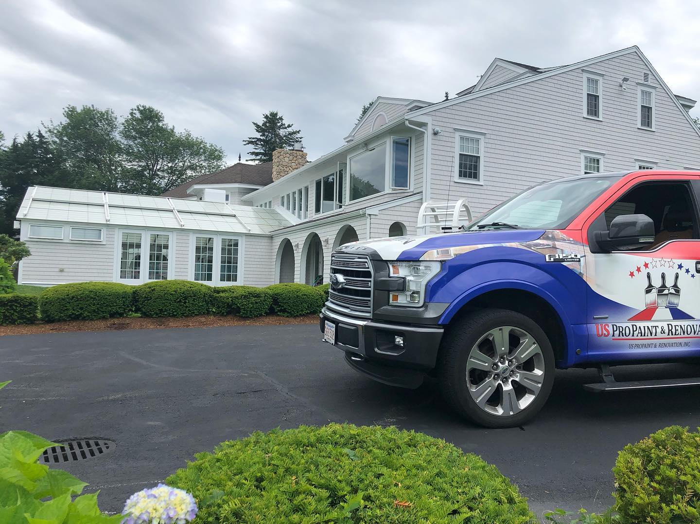 A blue and red truck parked in front of a large white house with a manicured lawn.