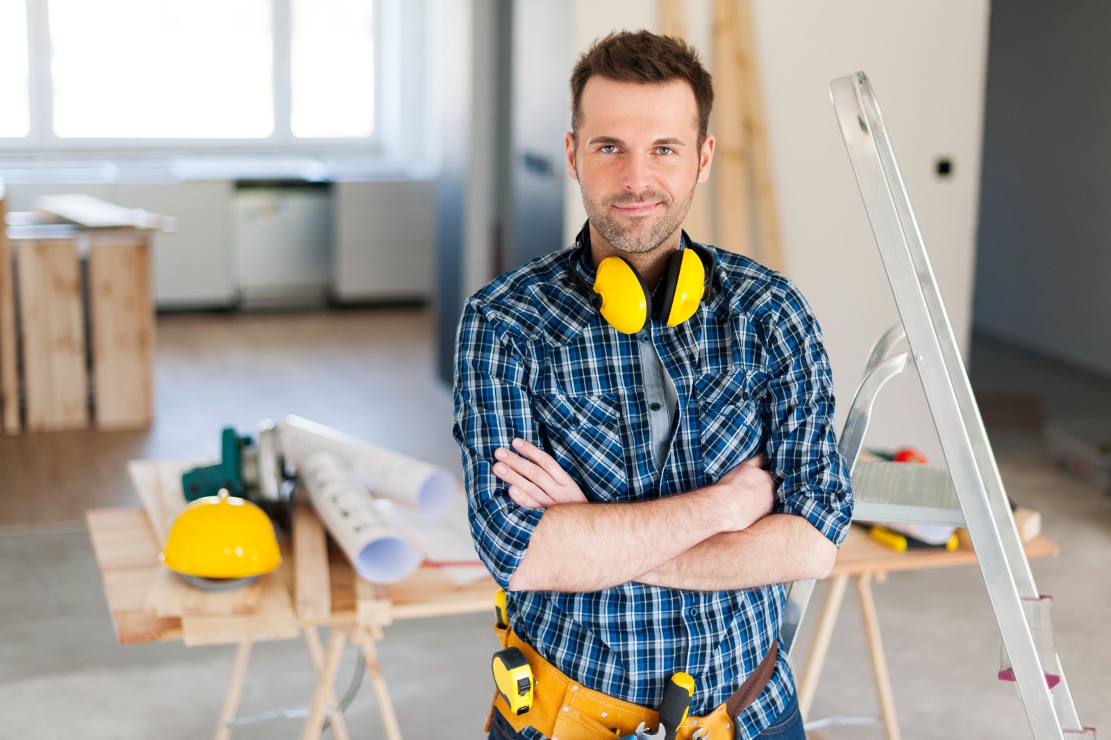Confident construction worker with safety gear stands with arms crossed.